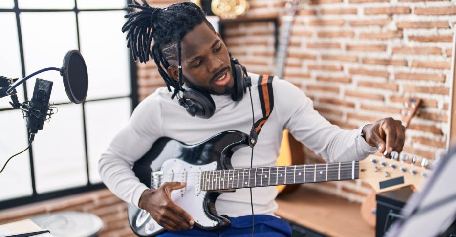 Ein Mann sitzt mit einer E-Gitarre auf einem Hocker