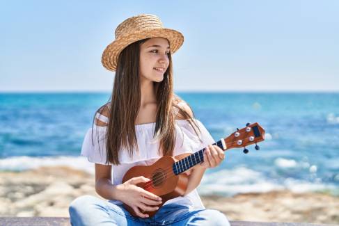Junge Frau mit einer Ukulele am Strand